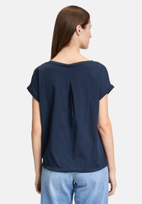 Granatowa koszula z krótkim rękawem o luźnym kroju, okrągłym dekolcie i detalach w postaci zakładki z tyłu. Wykonana z miękkiego materiału, lekko opada.
