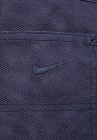 Sötétkék anyag, finom textúrával, a jobb oldalon egy hímzett fekete Nike logóval, valamint látható varrási részletekkel.