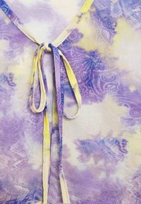 Sheer, lightweight purple fabric with yellow and blue accents; features a V-neck with ties at the center for adjustable fit.