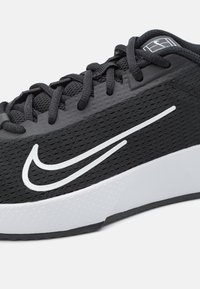 Chaussure de sport noire avec tige en mesh, logo Nike blanc et semelle intermédiaire blanche contrastante. Équipée de lacets noirs et de détails texturés.
