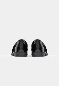 Scarpe in pelle verniciata nera con punta arrotondata, tacco basso e finitura lucida e elegante con dettagli di cucitura discreti.