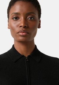 Black textured zip-up jacket with a collared neck. Zipper features a small metallic accent. Fabric appears soft and warm.