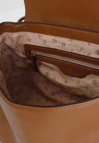 Vnitřek hnědé kožené kabelky s hladkým textilním podšívkou a jemným opakujícím se vzorem loga, včetně kapsy na zip.