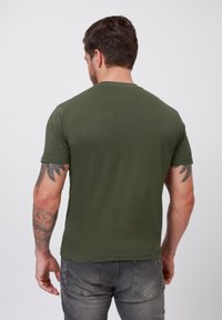 Olivengrøn kortærmet t-shirt med rund halsudskæring, glat tekstur og tætsiddende design, parret med grå bukser.