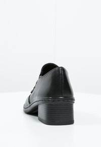 Black leather heel shoe with a rounded toe, braided leather accent along the sole, and a low block heel. Simple and smooth texture.