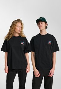 Zwarte katoenen T-shirts met korte mouwen en een relaxte pasvorm. Voorzien van een kleurrijk grafisch logo op het bovenste linkerdeel van de borst.