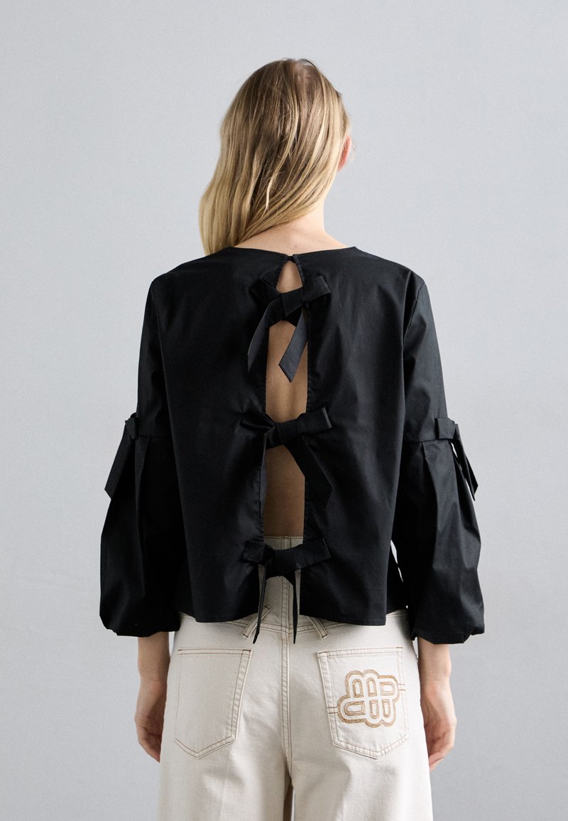 Čierny skrátený top s okrúhlym výstrihom, dlhými rukávmi a viacerými stuhami na chrbte, ktoré odhaľujú pokožku cez výrezy.