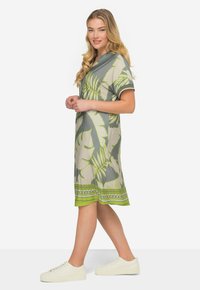 Sukienka z krótkim rękawem w kolorze szarym z zielonym tropikalnym wzorem liści, z okrągłym dekoltem i wzorzystym dołem, zestawiona z białymi sneakersami.