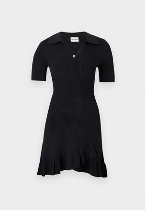 Γυναίκα που φοράει κοντό μαύρο φόρεμα με βολάν στο τελείωμα, μαύρα φλατ παπούτσια, κρίκους σκουλαρίκια και κρατάει καφέ δερμάτινη τσάντα ώμου.