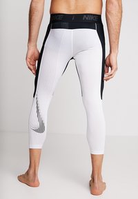 White athletic leggings with black accents, featuring a textured waistband and vertical striped pattern. Nike logo displayed on the thigh.
