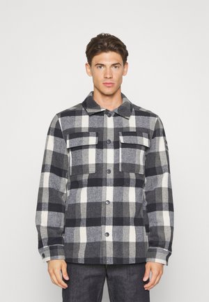 Plaid flannel jacket in gray, black, and white. Features two chest pockets, button closure, and a classic collar. Soft texture.