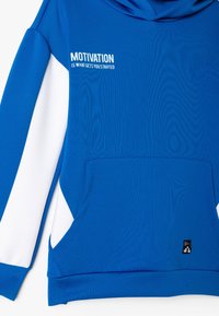 Sudadera azul con detalles en blanco, que presenta un bolsillo canguro y el texto "LA MOTIVACIÓN ES LO QUE TE HACE EMPEZAR" en el frente. Textura suave.