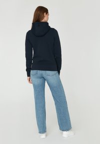 Sudadera con capucha de color azul marino, con cordón y bolsillo tipo canguro, combinada con jeans de pierna ancha de color azul claro y zapatillas blancas.