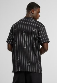 Black short-sleeve shirt with white vertical stripes and small white graphic designs. Relaxed fit with a rounded neckline and straight hem.