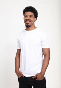White crew-neck t-shirt made of cotton, featuring short sleeves and a relaxed fit. Worn with black jeans. Smooth texture, minimal design.