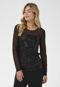 Top nero a maniche lunghe con corpetto a paillettes e maniche in rete trasparente, caratterizzato da un colletto rotondo e una silhouette leggermente aderente.