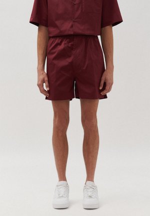 Pantaloni corti borgogna realizzati in tessuto leggero con vita elasticizzata. Taglio dritto con spacchi laterali per facilitare i movimenti. Sneakers bianche.