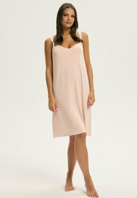 Jasnoróżowa, bezrękawnikowa sukienka z dekoltem w kształcie litery V, gładki materiał, długość do kolan i subtelne ramiączka. Brak widocznych wzorów lub zapięć.