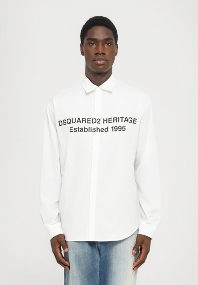 Bijela košulja dugih rukava s ovratnikom na gumbe, na prednjoj strani s crnim ispisanim tekstom "DSQUARED2 HERITAGE Osnovan 1995".