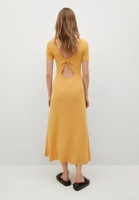 Robe en tricot jaune à manches courtes et détail de dos nu, ornée d'un nœud torsadé. Le tissu est lisse et la jupe arrive au mi-mollet.