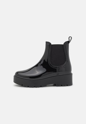 Bottines noires brillantes avec des panneaux latéraux élastiques, une tirette et une semelle en caoutchouc épaisse. Surface lisse sans motifs ni accessoires visibles.
