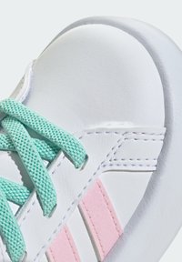 Sneaker in pelle bianca con lacci verde menta, strisce rosa di accento e punta rotonda. Texture liscia con dettagli cuciti.