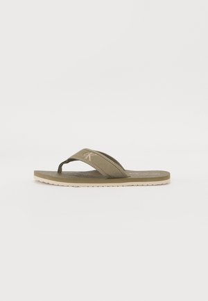 Brune flip-flop med canvasrem, som har en strukturert såle og gummisåle. Enkel design med et minimalistisk logo.