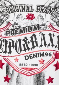 Weißes T-Shirt mit auffälligem Grafikdesign, schwarzem und rotem Text, Sternen sowie Illustrationen eines Tigers und Schlangen.