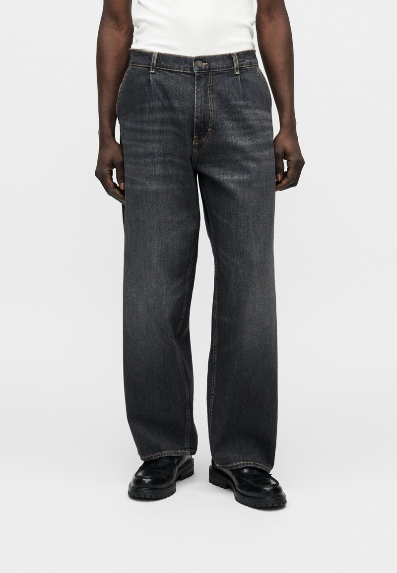 Σκούρο τζιν παντελόνι με ευρύ πόδι και ίσια γραμμή, με κούμπωμα κουμπιού και φερμουάρ, και εμφανείς αντιθετικές ραφές.