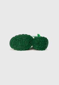 Suola verde di una sneaker con profonde scanalature per aderenza, caratterizzata da motivi testurizzati e dettagli bianchi vicino al midsole.