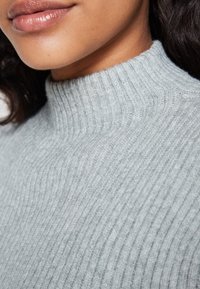 Maglione a collo alto lavorato a coste di un grigio chiaro, con una superficie testurizzata e sottili linee verticali.