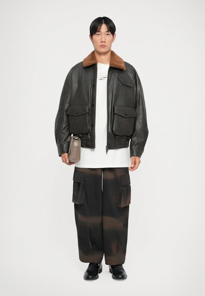 Black leather bomber jacket with a brown fur collar, white t-shirt, and black cargo pants with brown stripes. Slim, round-toed black shoes.