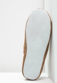 Chaussure en daim marron avec une semelle grise lisse, présentant un bout rond et une surface texturée. Le design met l'accent sur le confort et la simplicité.
