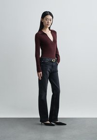 Bordo spalvos ilgomis rankovėmis palaidinė su V formos iškirpte, derinama su juodais aukšto liemens džinsais ir juodais kulniukais su aštriu priekiu; lygios tekstūros ir prigludusio dizaino.