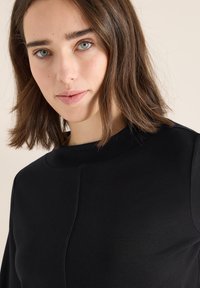 Black garment with a high neckline and long sleeves, featuring a smooth texture and seam detailing on the front.