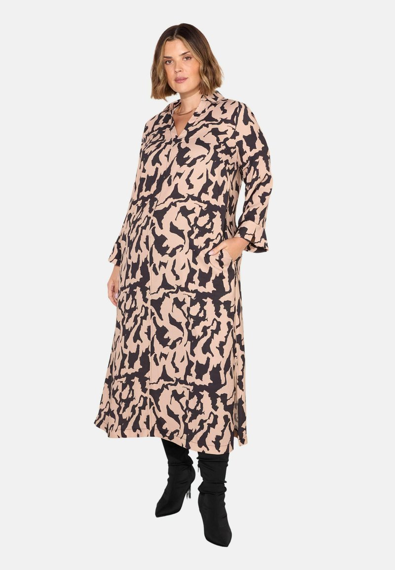 Abito a maniche lunghe, di lunghezza media, beige con un motivo astratto nero. Presenta un colletto e tasche laterali, abbinato a stivali neri al ginocchio.