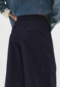 Pantaloni cargo blu navy realizzati in tessuto morbido con tasche laterali e una vestibilità comoda, abbinati a una giacca di jeans.