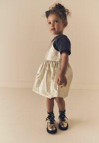 Metallisk silverfärgad klänning med en rynkad kjol, ihopparad med svarta kortärmar. Svart och guld snörda stövlar fulländar outfiten.