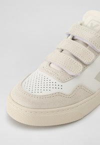 Lys beige sneaker med overdel i semsket skinn og lær, med perforert design, borrelåsremmer og teksturert gummisåle.