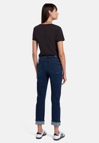 Jeans in denim blu scuro con orli risvoltati, design a cinque tasche e cuciture a contrasto, abbinati a una maglietta nera a maniche corte.