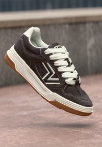 Baskets en daim noir avec des lacets blancs, une semelle blanche et une semelle extérieure en caoutchouc marron. Présentent un logo latéral blanc et gris et des détails perforés.