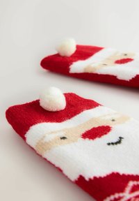 Červené huňaté ponožky s motivem Santy, bílé pom-pom detaily a kontrastní černé oči na měkkém, texturovaném povrchu.