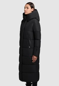 Černá péřová bunda s vysokým límcem, dlouhého střihu, s kapsami na zip a boxovitým designem s prošívanou texturou.