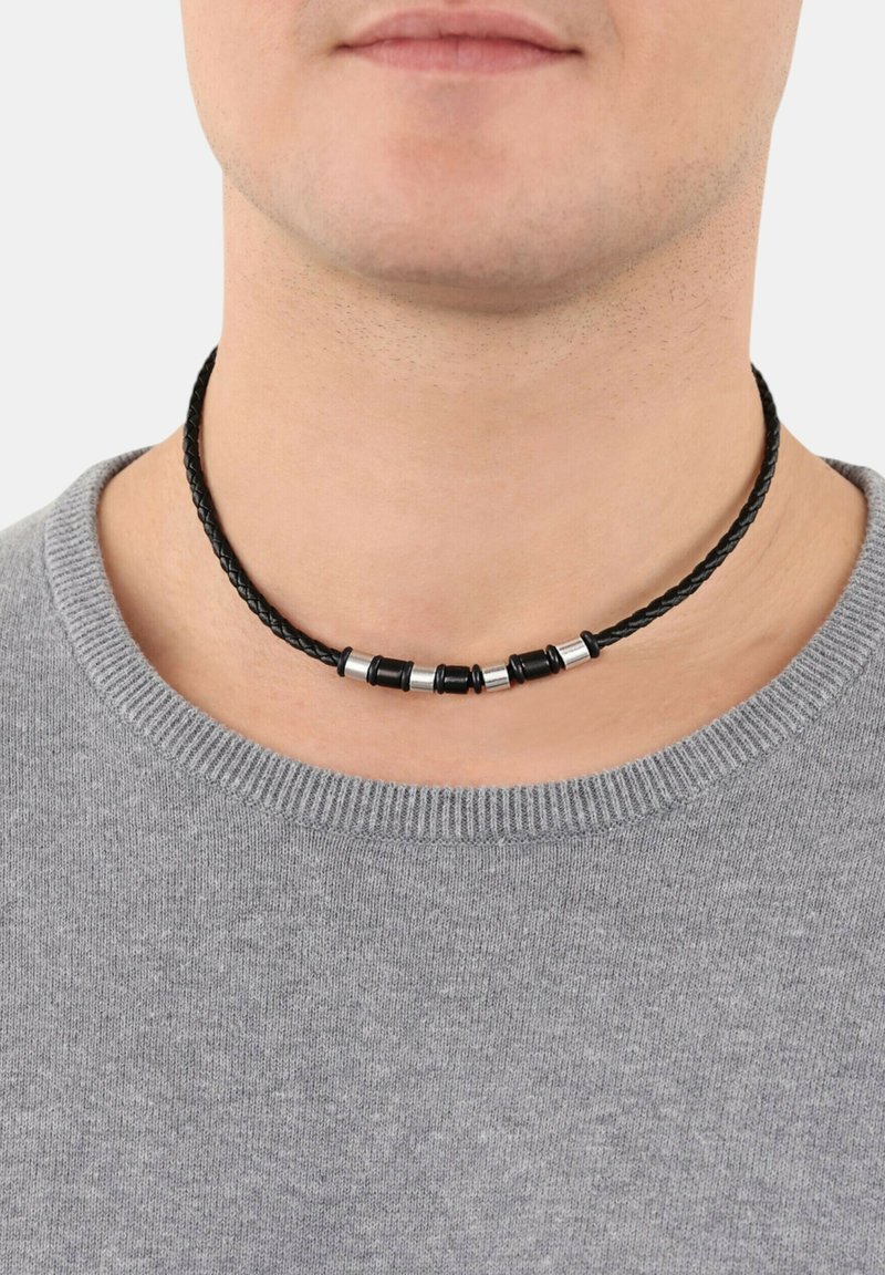 Geflochtener schwarzer Lederchoker mit metallischen Perlenakzenten in Silber und Schwarz, um den Hals getragen, über einem grauen Pullover mit Rundhalsausschnitt.