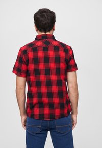 Camisa de cuadros de manga corta en rojo y negro, hecha de un tejido con un patrón a cuadros. Cuenta con un cuello clásico y un corte informal.