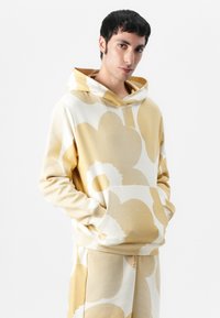 Kapuzensweatshirt aus weichem Stoff mit großen creme- und beigefarbenen Blumenmustern, Kängurutasche und Tunnelzugkapuze.