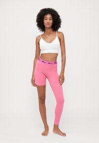 Roze tajice s visokim strukom koje imaju crne logotip akcenta, uparene s bijelim sportskim grudnjakom. Glatka, rastezljiva tkanina.