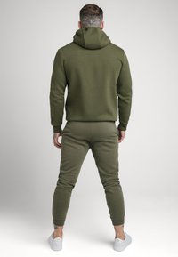 Olijfgroene sweat hoodie met een kangoeroezak, gecombineerd met bijpassende taps toelopende joggers. Zachte textuur, elastische manchetten en enkelopeningen.