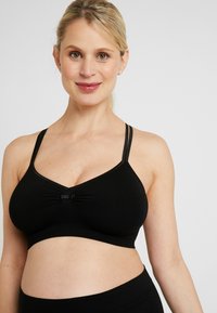 Zwarte bralette van zacht materiaal; heeft een V-hals, dubbele bandjes en een strikdetail in het midden. Gladde textuur met een rekbare pasvorm.