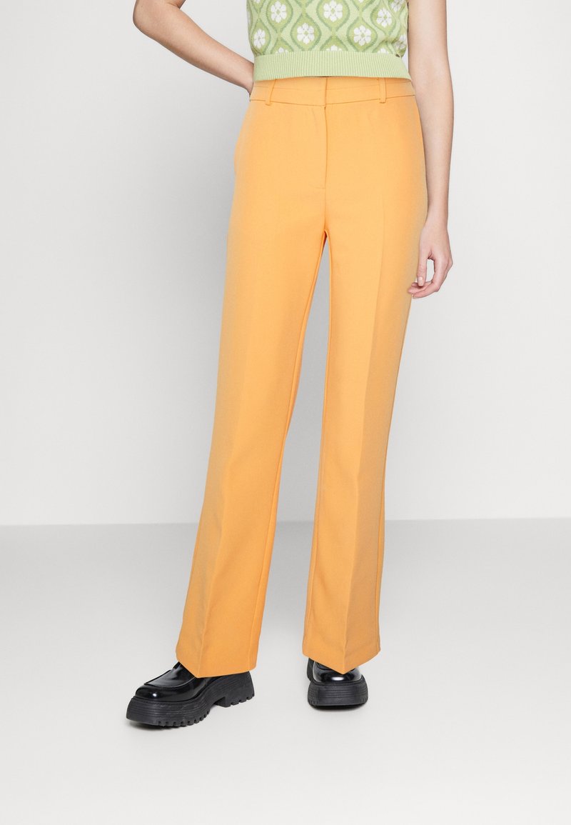 Pantalons orange à larges jambes en tissu lisse, dotés d'une taille haute et de lignes épurées. Associés à des chaussures à plateforme noires robustes.